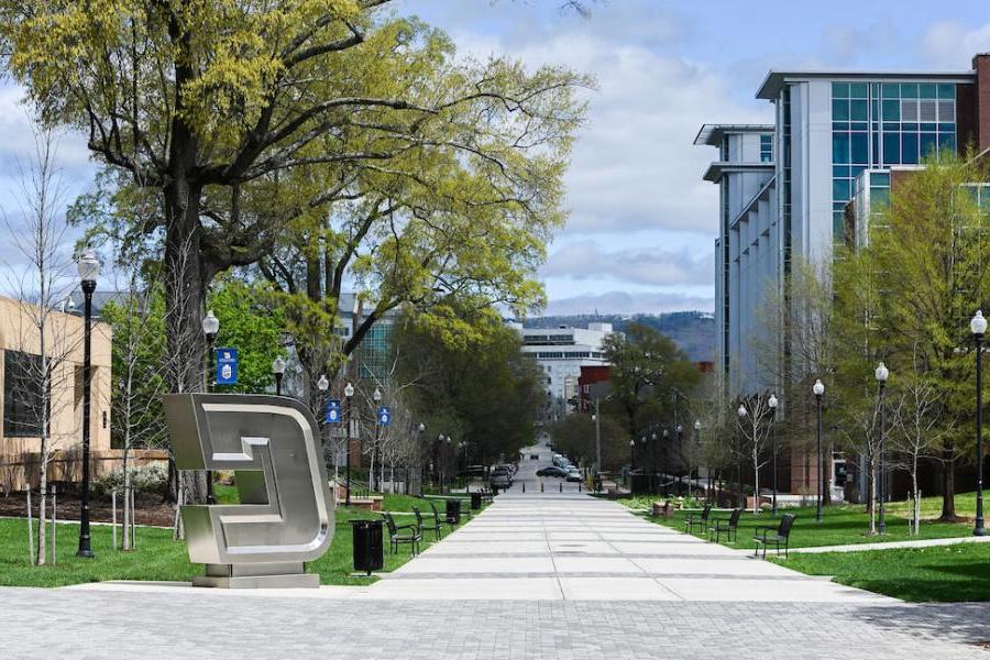 A view of the tree-lined Vine Street Pedestrian Mall on the UTC Campus, including the stainless-steel "Power C" logo sculpture, Derthick Hall and the UTC Library, with the Unum building in the background.